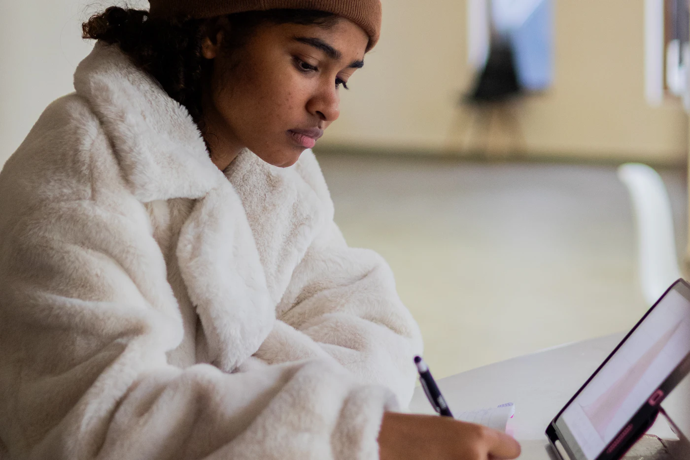 A young designer writing notes at a table, with a tablet beside her